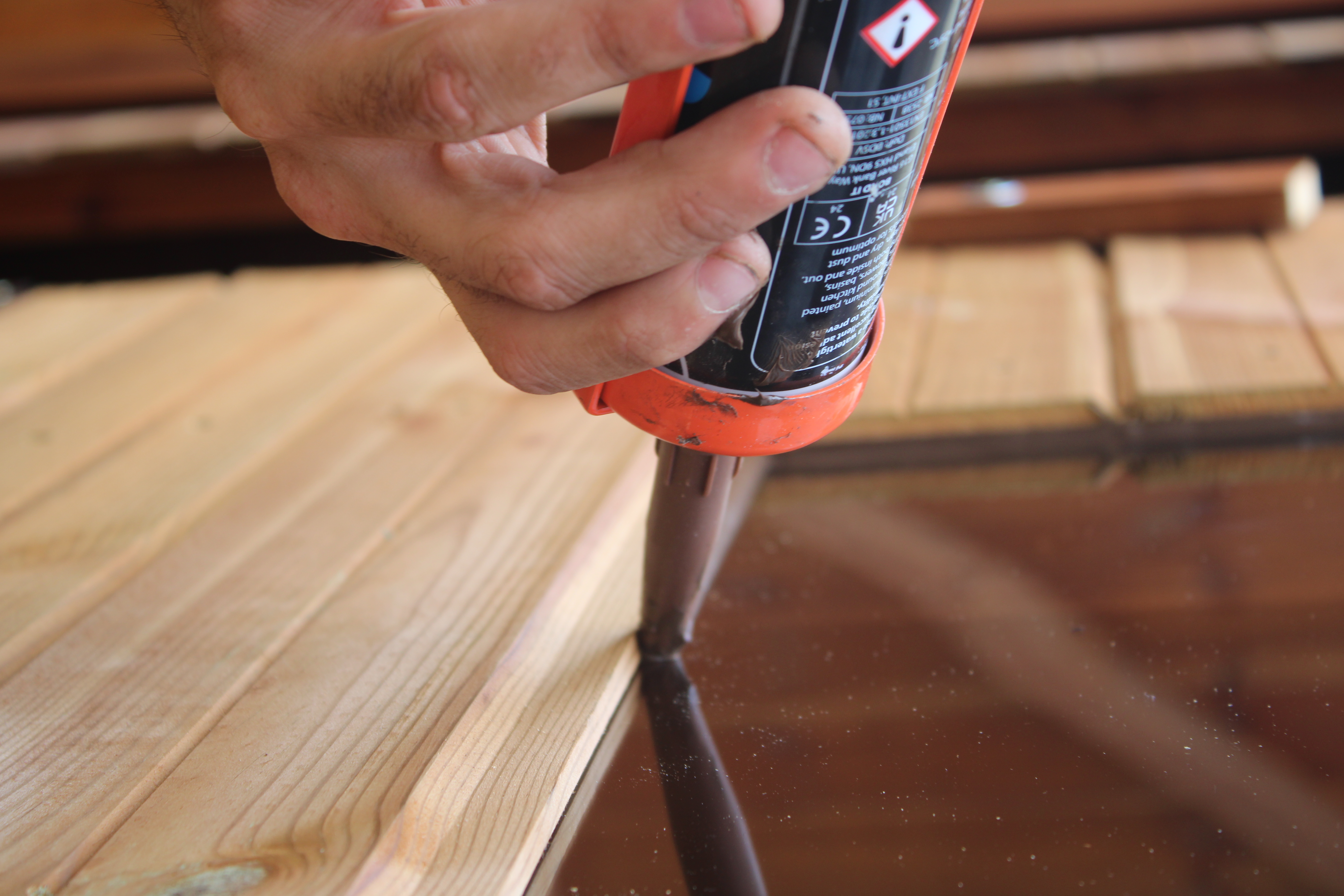 Spartan Sheds installer applying silicone sealant to a window during shed installation